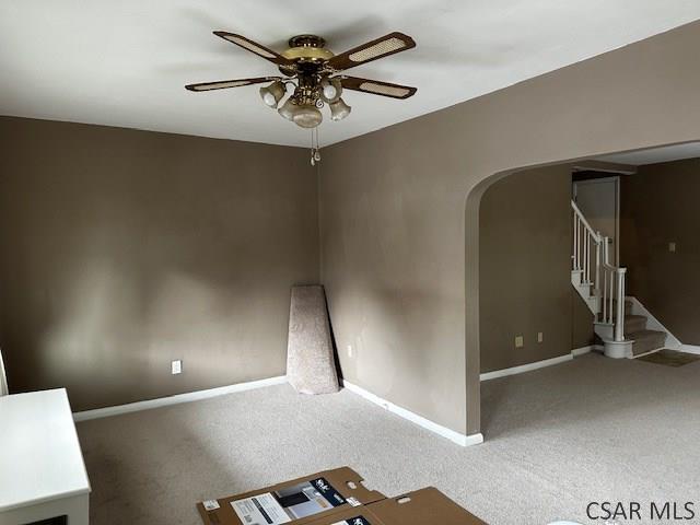 carpeted spare room with arched walkways, ceiling fan, stairway, and baseboards