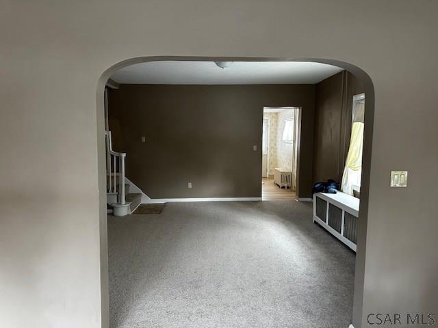 unfurnished room with arched walkways, stairway, baseboards, and radiator