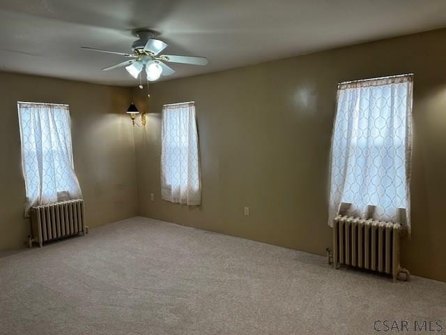 empty room with ceiling fan, light colored carpet, and radiator