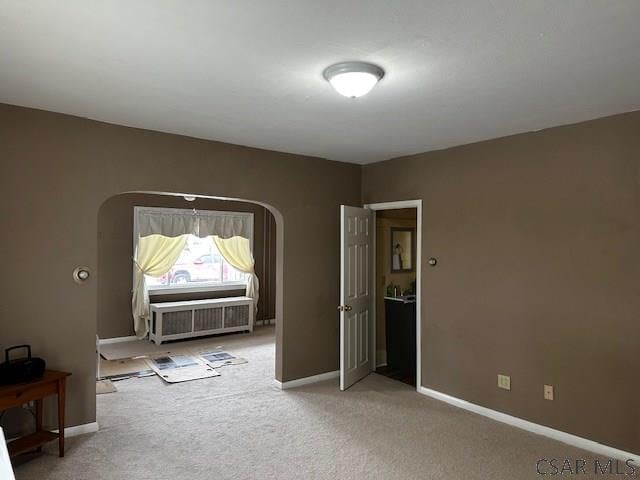 spare room featuring arched walkways, light colored carpet, and baseboards