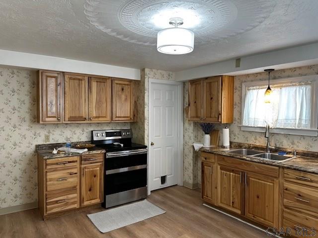 kitchen featuring wallpapered walls, electric stove, dark countertops, brown cabinets, and a sink