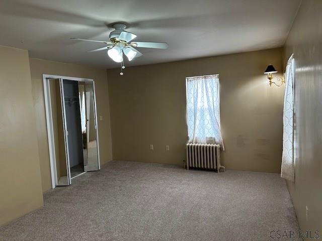 empty room with light carpet, radiator heating unit, and ceiling fan