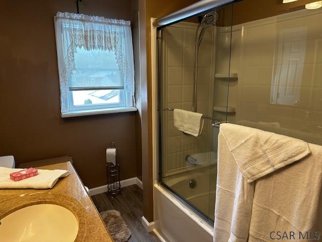 full bathroom with shower / bath combination with glass door, wood finished floors, vanity, and baseboards