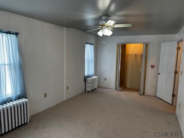 unfurnished bedroom with radiator, light carpet, and ceiling fan