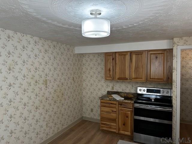 kitchen with wallpapered walls, stainless steel electric range, and brown cabinetry