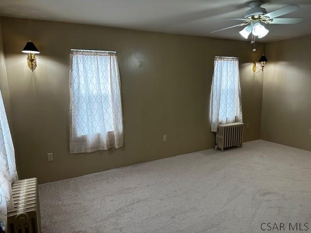 carpeted empty room featuring ceiling fan, plenty of natural light, and radiator