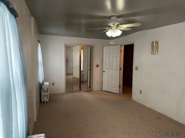 unfurnished bedroom with light carpet, ceiling fan, radiator heating unit, and a closet