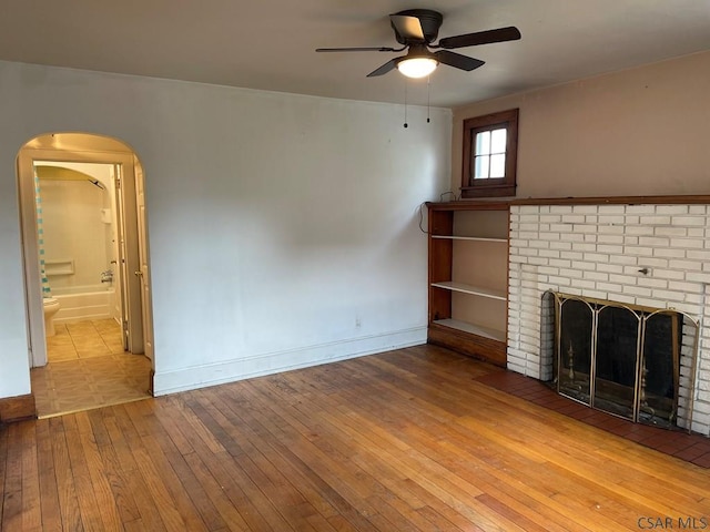 161 Stone St, Johnstown, PA 15906 - unfurnished living room featuring hardwood / wood-style floors, ceiling fan, arched walkways, baseboards, and a brick fireplace