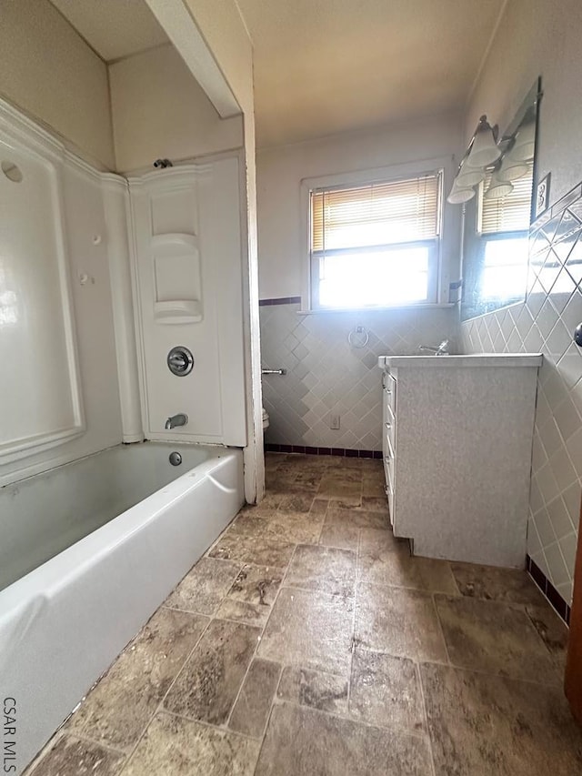 bathroom featuring toilet, vanity, tile walls, shower / washtub combination, and stone finish flooring