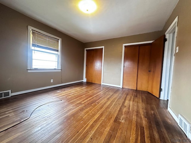 unfurnished bedroom featuring baseboards, wood-type flooring, visible vents, and multiple closets