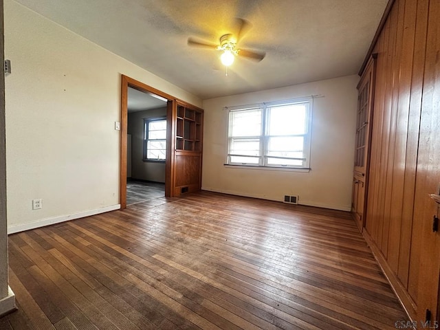 unfurnished room featuring dark wood-style flooring, visible vents, ceiling fan, and baseboards