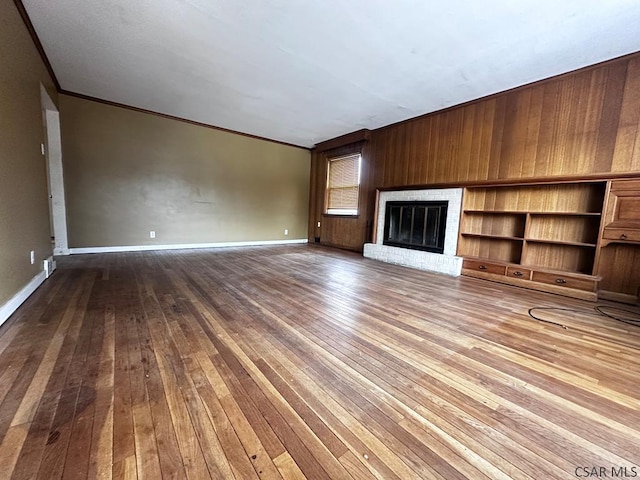 unfurnished living room featuring ornamental molding, a brick fireplace, hardwood / wood-style flooring, and baseboards