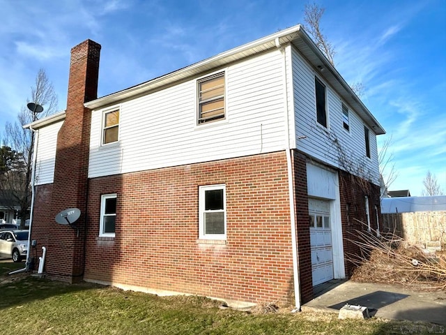 view of side of property featuring a garage, brick siding, and a chimney