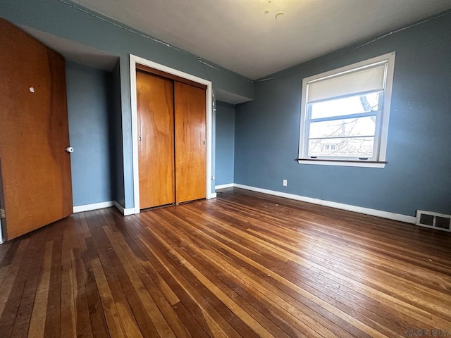 unfurnished bedroom featuring dark wood-style floors, a closet, visible vents, and baseboards