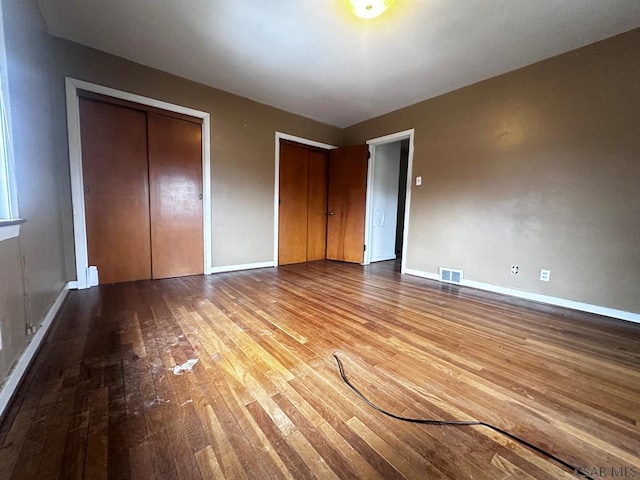 unfurnished bedroom with hardwood / wood-style floors, two closets, visible vents, and baseboards