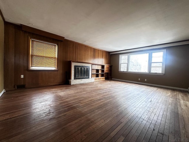 unfurnished living room featuring visible vents, a brick fireplace, wooden walls, baseboards, and hardwood / wood-style flooring