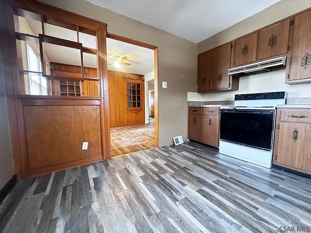 kitchen with under cabinet range hood, light countertops, electric range oven, and wood finished floors