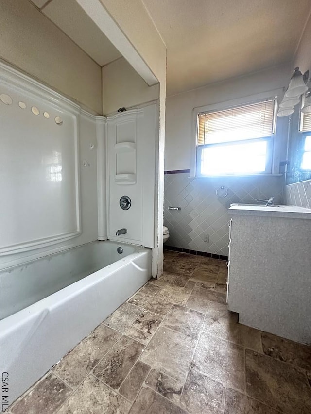 bathroom featuring a wainscoted wall, tile walls, bathtub / shower combination, toilet, and stone finish flooring