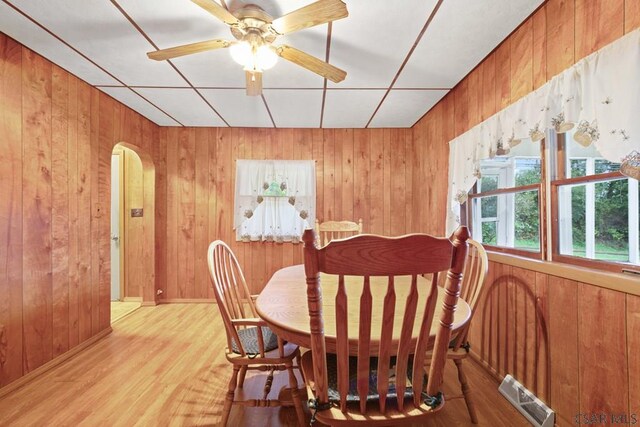 dining space with light hardwood / wood-style flooring, wooden walls, and ceiling fan