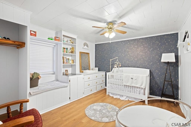 bedroom featuring light hardwood / wood-style floors, ornamental molding, a nursery area, and ceiling fan