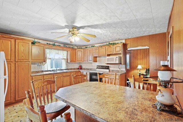 kitchen with sink, white appliances, ceiling fan, and wood walls