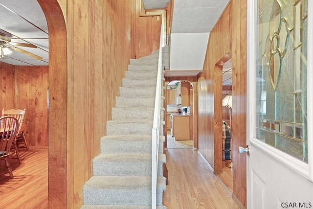 stairs with ceiling fan, wooden walls, and hardwood / wood-style floors