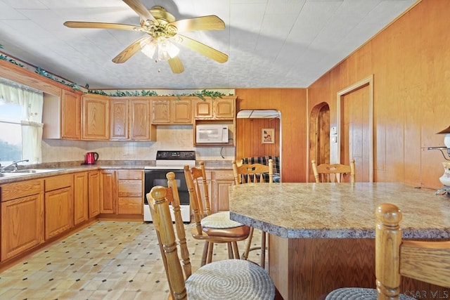 kitchen featuring a breakfast bar, sink, wood walls, white appliances, and ceiling fan