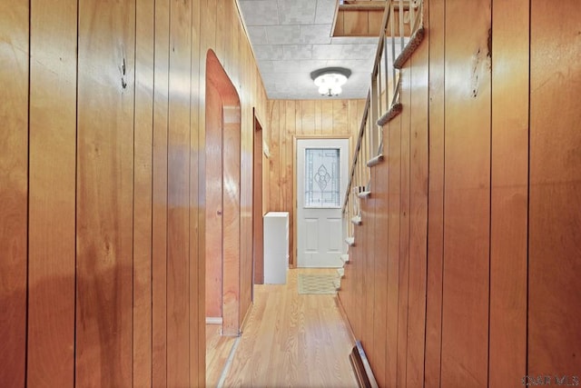 hall with light wood-type flooring and wood walls