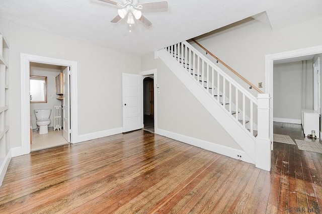 unfurnished living room featuring ceiling fan, stairway, hardwood / wood-style flooring, and baseboards