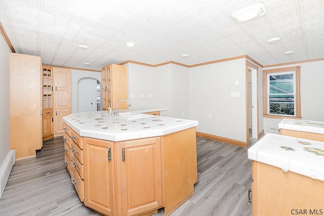 kitchen featuring tile counters, arched walkways, light wood-style flooring, a kitchen island with sink, and a sink