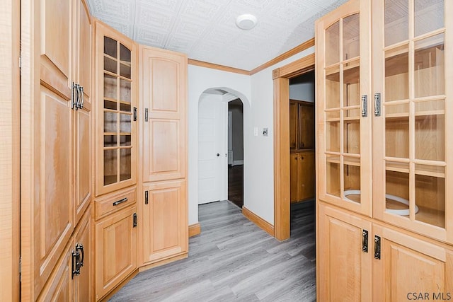 corridor featuring an ornate ceiling, arched walkways, light wood-style flooring, ornamental molding, and baseboards