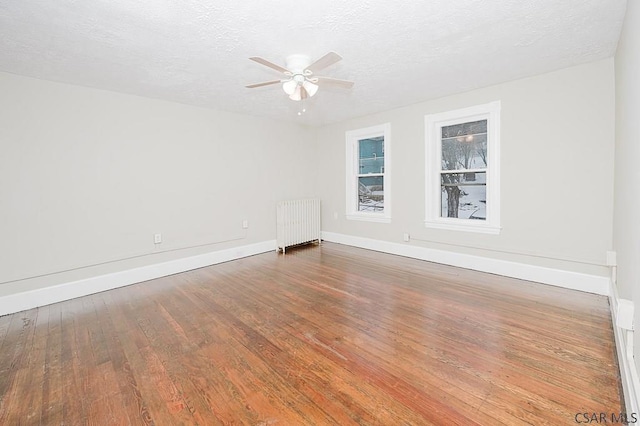 empty room featuring a textured ceiling, ceiling fan, wood finished floors, baseboards, and radiator