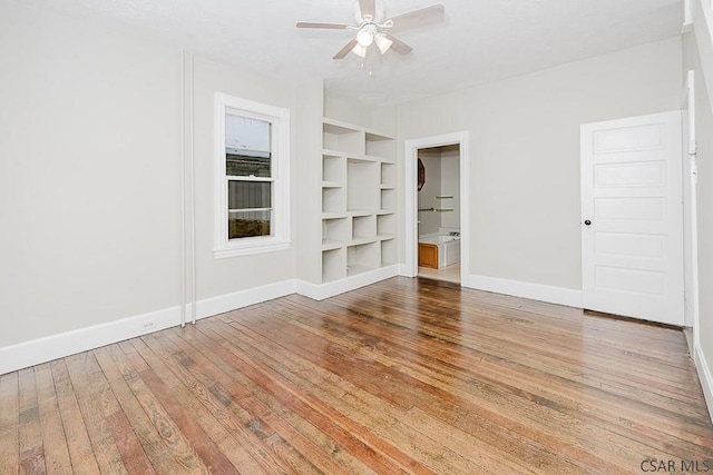 unfurnished room with wood-type flooring, built in shelves, baseboards, and ceiling fan