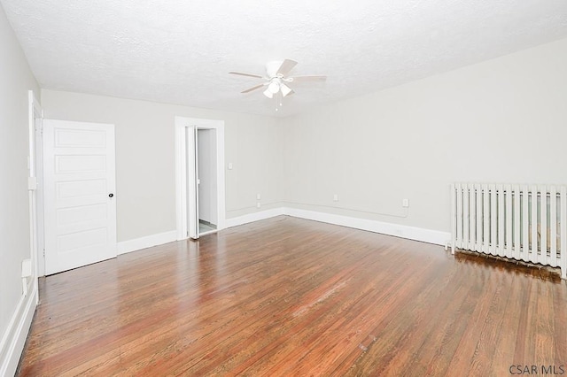 spare room featuring a textured ceiling, wood finished floors, a ceiling fan, baseboards, and radiator heating unit