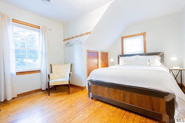 bedroom featuring baseboards, light wood-style flooring, and lofted ceiling