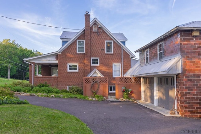 view of front of home featuring brick siding, driveway, a chimney, and metal roof