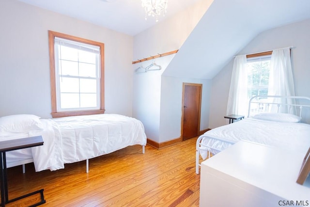 bedroom featuring light wood-style floors, baseboards, lofted ceiling, and a chandelier