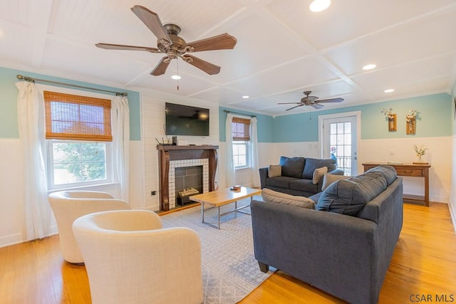 living room featuring coffered ceiling, ceiling fan, a wainscoted wall, and a wealth of natural light