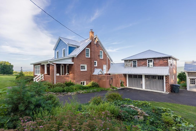view of front of property featuring a chimney, metal roof, a garage, brick siding, and aphalt driveway