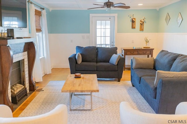 living room featuring a ceiling fan, a fireplace with flush hearth, crown molding, wood finished floors, and a wainscoted wall