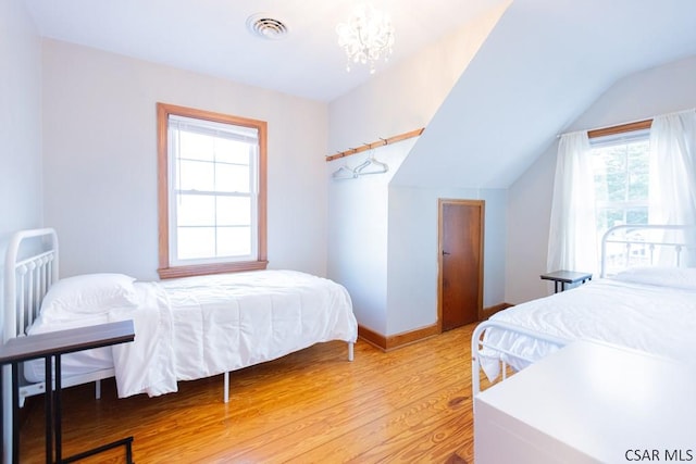 bedroom featuring visible vents, vaulted ceiling, light wood-type flooring, baseboards, and an inviting chandelier