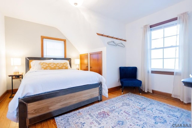 bedroom with baseboards, vaulted ceiling, and wood finished floors