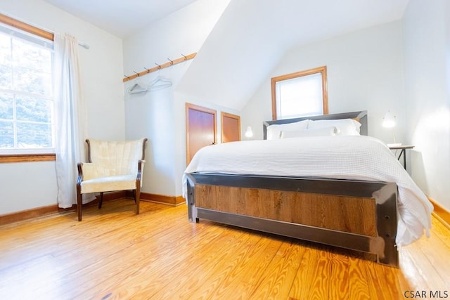 bedroom with light wood-style floors, baseboards, multiple windows, and lofted ceiling