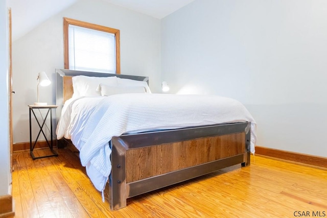 bedroom with baseboards, vaulted ceiling, and wood finished floors
