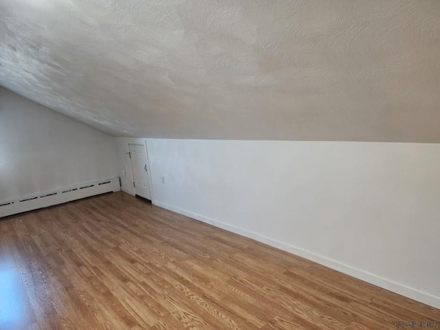 additional living space with a baseboard radiator, light hardwood / wood-style flooring, and a textured ceiling