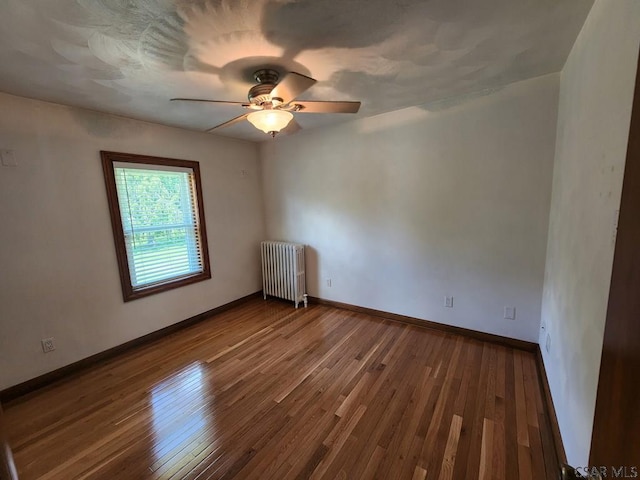 empty room featuring hardwood / wood-style flooring, ceiling fan, and radiator