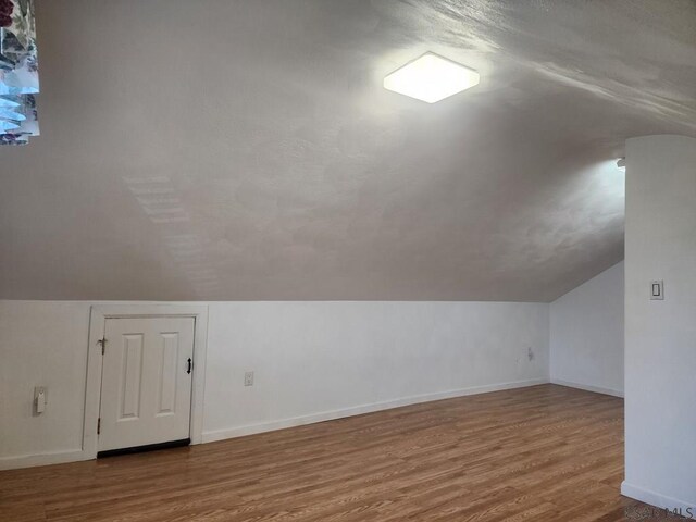 additional living space with hardwood / wood-style floors and vaulted ceiling