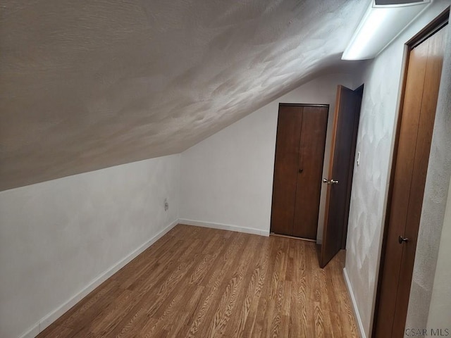 additional living space with vaulted ceiling and light hardwood / wood-style flooring