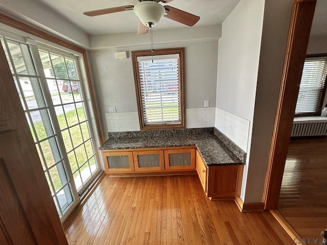 unfurnished dining area with radiator heating unit, ceiling fan, a wealth of natural light, and light hardwood / wood-style floors