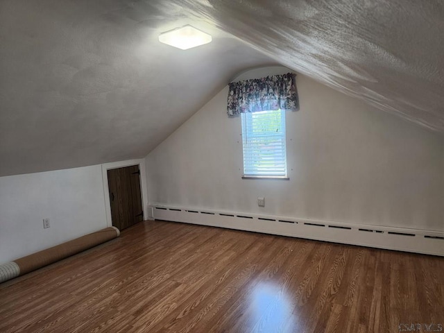 additional living space featuring lofted ceiling, wood-type flooring, and a baseboard heating unit